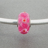 Pink murano glass bead with pink spinner pattern on a silver bangle against a grey background