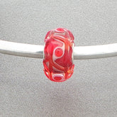 Red glass bead with a tactile design and white core on a silver bangle against a grey background