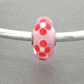 Pink glass bead with red floral patterns on a silver metal bar against a gray background