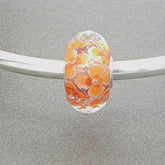 Faceted glass bead with orange floral pattern on a silver bangle against a grey background