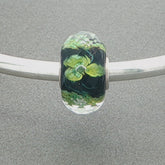 Faceted glass bead with green floral design and sprinkle of gold glitter on a grey background