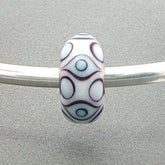 Decorative white opaque bead with eye design on a silver bangle against a grey background