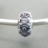 Decorative opaque white glass bead with eye pattern on a silver bangle against a grey background