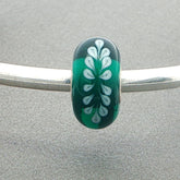 Green bead with white leafy pattern on a silver bangle against a grey background