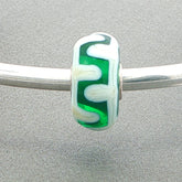 Green and white glass bead on a silver bangle against a grey background