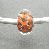 Glass faceted bead with orange and brown pattern on a silver bangle against a grey background