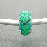 Green leafy patterned bead on a silver bangle against a grey background