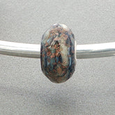 Decorative faceted glass bead with speckled pattern on a silver bangle against a grey background