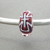 Glass bead with a white cross design on a silver bangle against a grey background