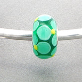 Green petal patterned bead on a silver bangle against a grey background