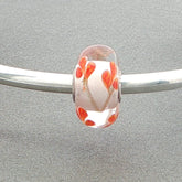 Glass bead with orange petals and golden stems on a silver bangle against a grey background