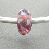 Mauve and white twirling petal patterned glass bead on a silver bangle against a grey background