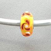 Glass bead with orange and yellow swirl pattern on a silver bangle against a grey background