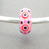 Murano glass bead with pink opaque core with pink and black dots with red circles on a silver bangle against a grey background