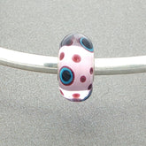 Polka dot murano glass bead with a pink core and burgundy dots with some with blue and black centres on a silver bangle against a grey background