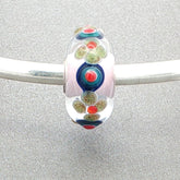 Colorful glass bead with floral and dot pattern on a silver bangle against a grey background