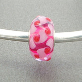 Murano glass bead with a pale pink and red design with a vibrant pink core on a silver bangle against a grey background