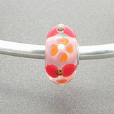 Glass bead with a floral design on a silver bangle against a grey background
