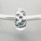 Murano glass bead with white core and glitter fan-like design on a silver bangle against a grey background
