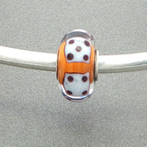 Murano glass bead with orange core and white dice design on a silver bangle against a grey background