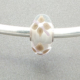 Murano glass bead with a white core and floral design on a silver bangle against a grey background