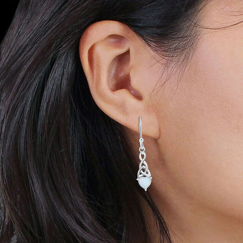 Close-up of an ear wearing a silver celtic trinity dangle earring with a dark background