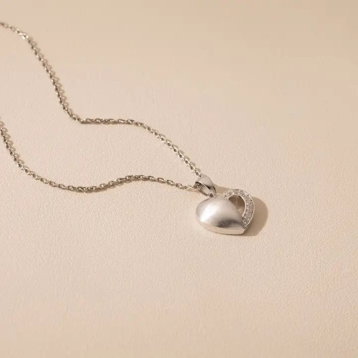 Silver heart-shaped pendant necklace on a beige background