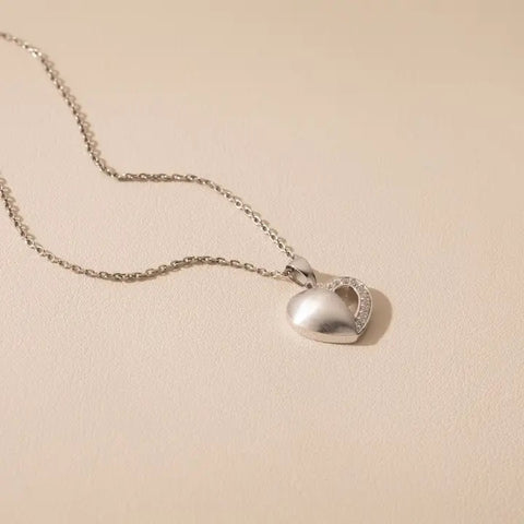 Silver heart-shaped pendant necklace on a beige background