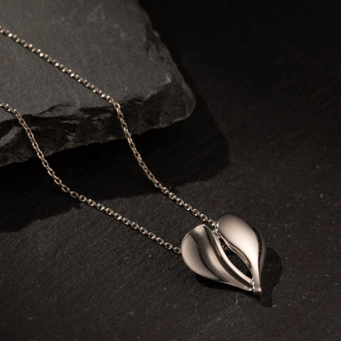 Silver leaf-shaped pendant on a chain against a dark stone background