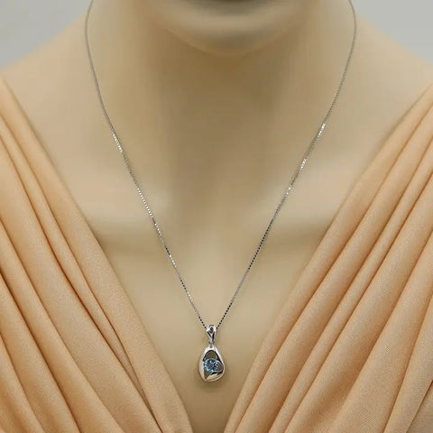 Silver necklace with a pendant on a mannequin wearing a beige dress.