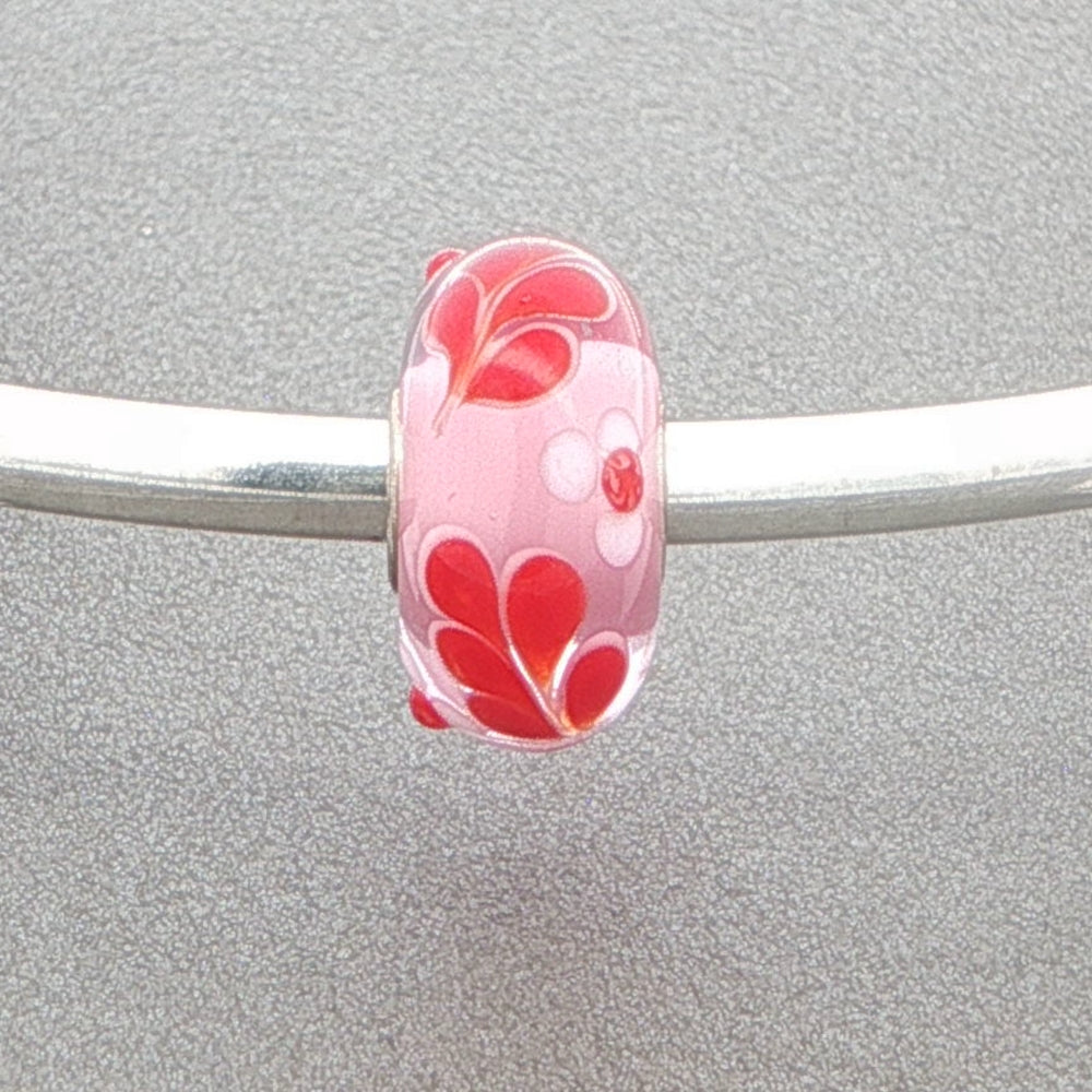 Red and white floral leaf with pink core murano glass bead on a silver bangle against a grey background