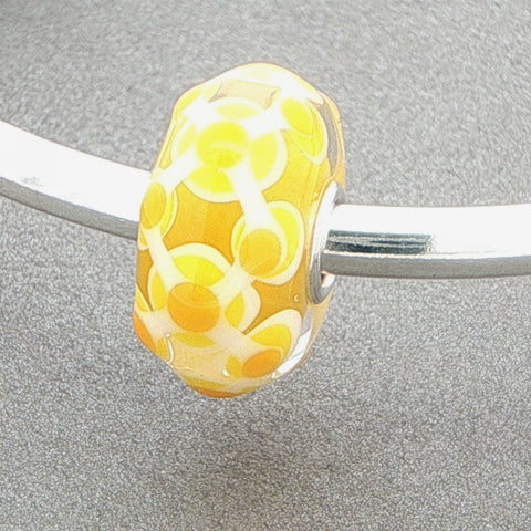 Yellow white designed glass bead on a silver bangle against a grey background