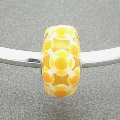 Yellow and white patterned murano glass bead on a silver bangle against a grey background
