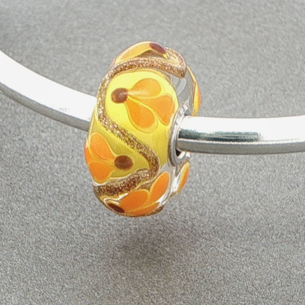 Decorative bead with floral pattern and glitter on a silver bangle against a grey background