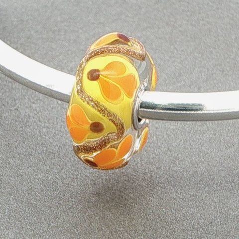 Decorative bead with floral pattern and glitter on a silver bangle against a grey background