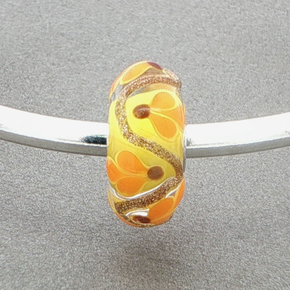 Yellow floral glass bead with glitter on a silver bangle against a grey background