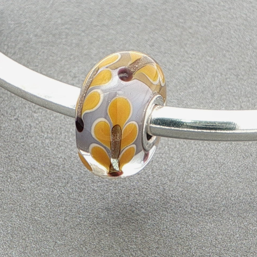 Silver bangle with a floral glass bead against a grey background