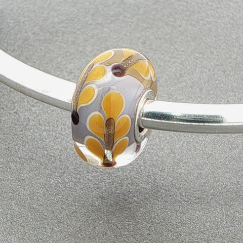 Silver bangle with a floral glass bead against a grey background