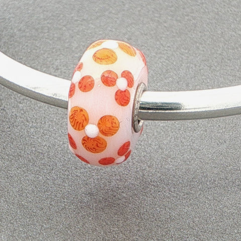 Bead with orange and white design on a silver bangle against a grey background