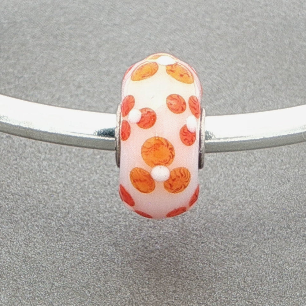 Murano glass bead with orange and white pattern on a silver bangle against a grey background