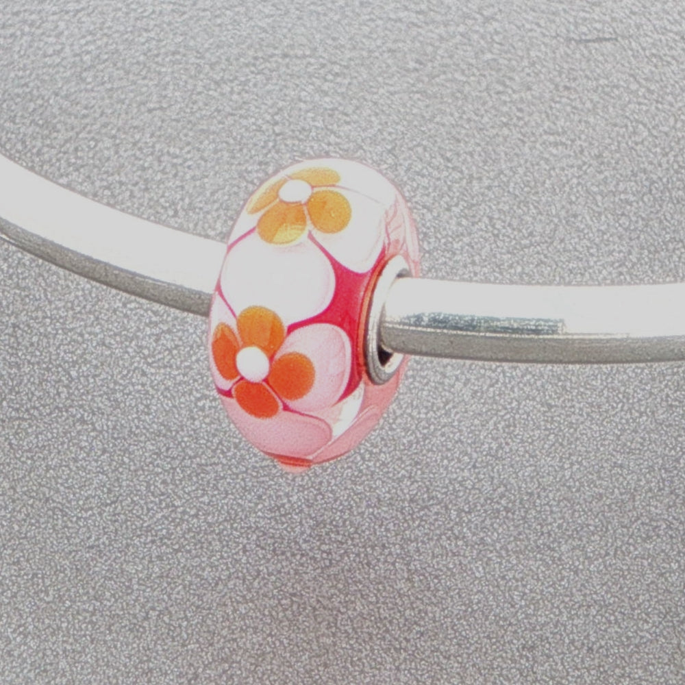Floral-patterned glass bead on a silver bangle against a grey background