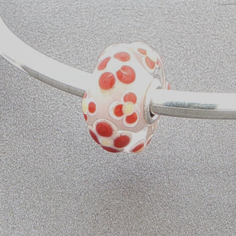 Glass bead with floral pattern on a silver bangle against a grey background