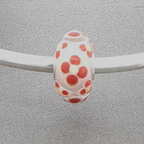 Glass bead with floral design on a silver bangle against a grey background