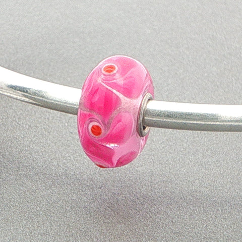 Pink glass bead with a pink design pattern on a silver bangle against a grey background
