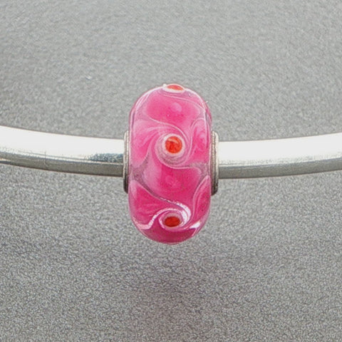 Pink murano glass bead with pink spinner pattern on a silver bangle against a grey background