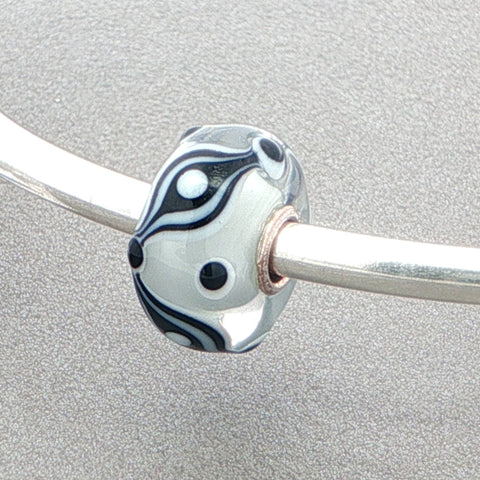 Glass bead with black and white pattern on a silver bangle against a grey background