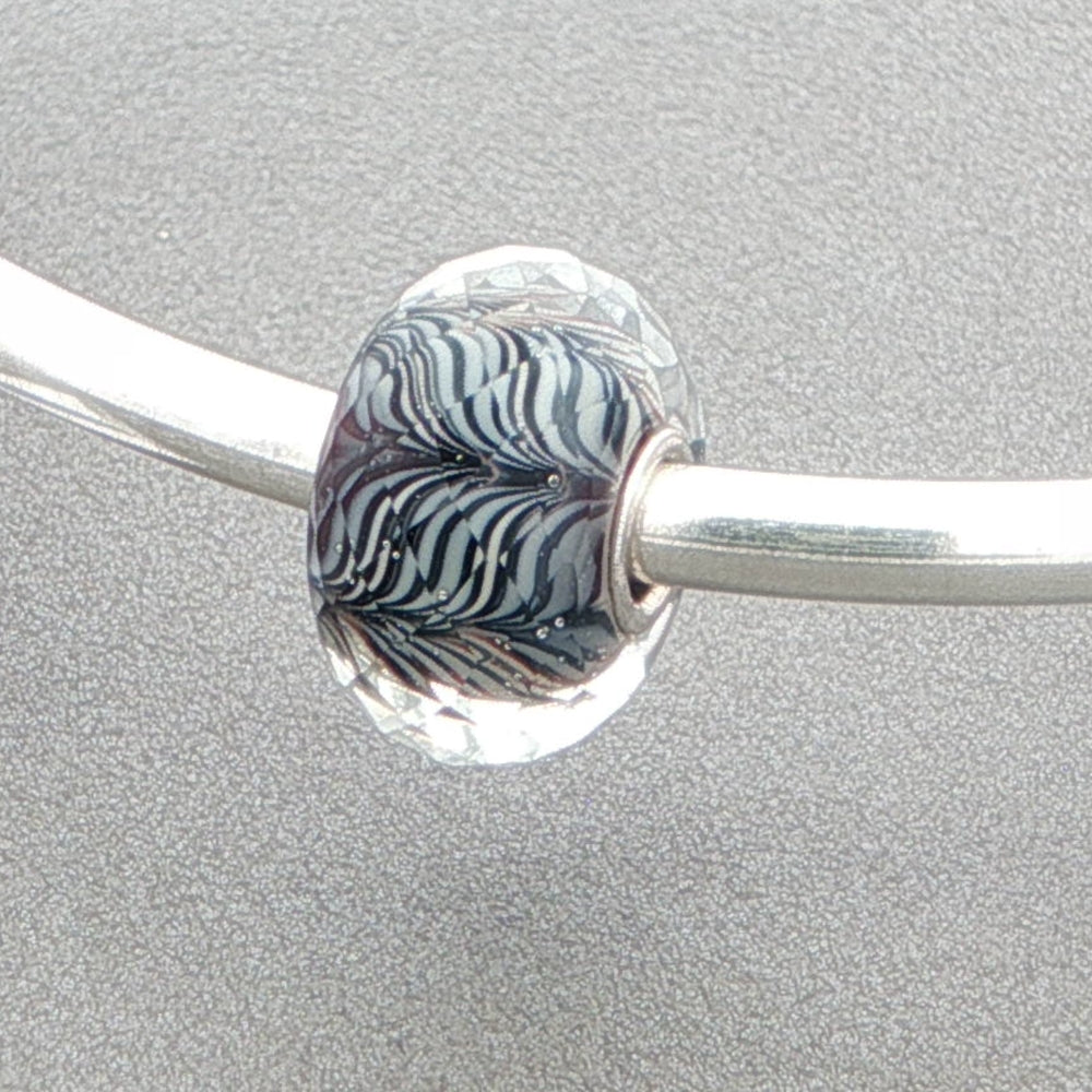 Faceted glass bead with a zebra-type pattern on a silver bangle against a grey background