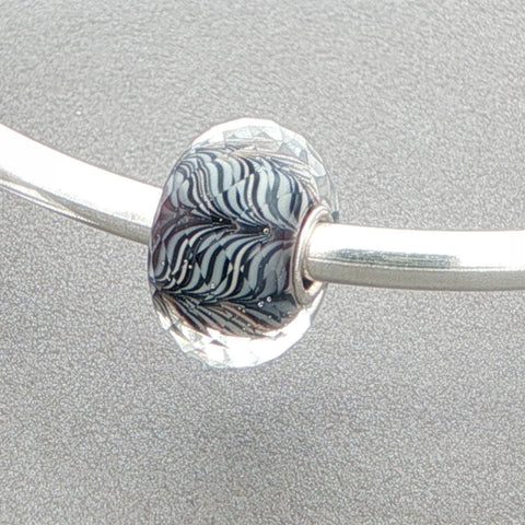 Faceted glass bead with a zebra-type pattern on a silver bangle against a grey background