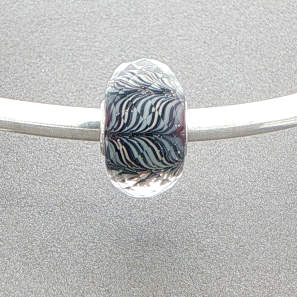 Silver bangle with a zebra-striped faceted glass murano bead against a grey background