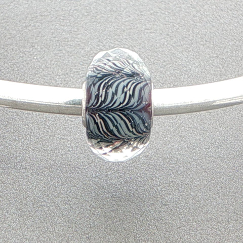 Silver bangle with a zebra-striped faceted glass murano bead against a grey background
